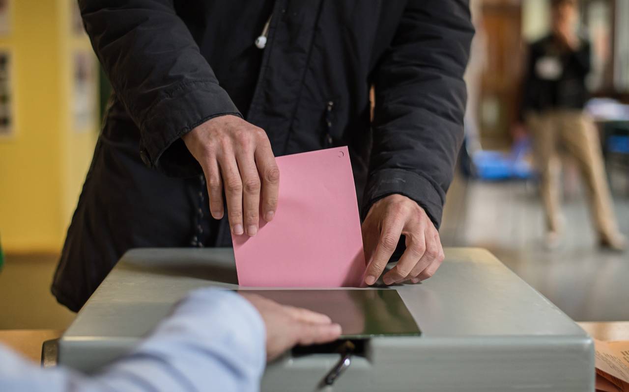 Ein Stimmzettel in einem Umschlag wird in eine Wahlurne eingeworfen.