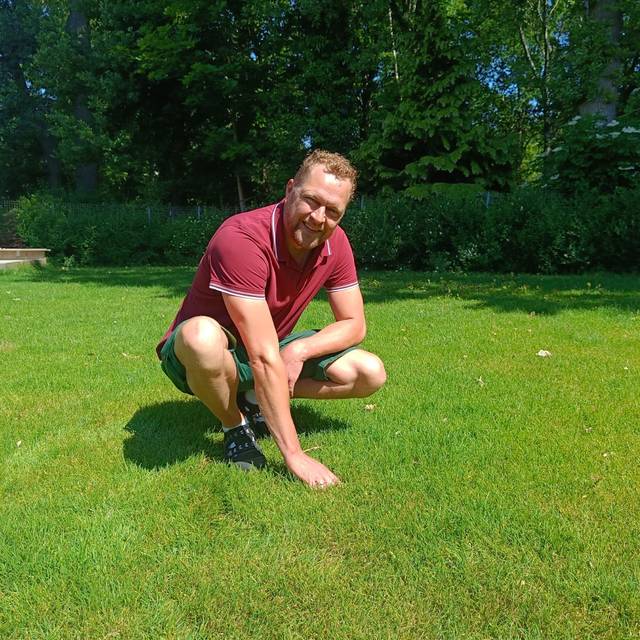 Gartenbauer Matthias Pölling zeigt auf dem Rasen im Garten