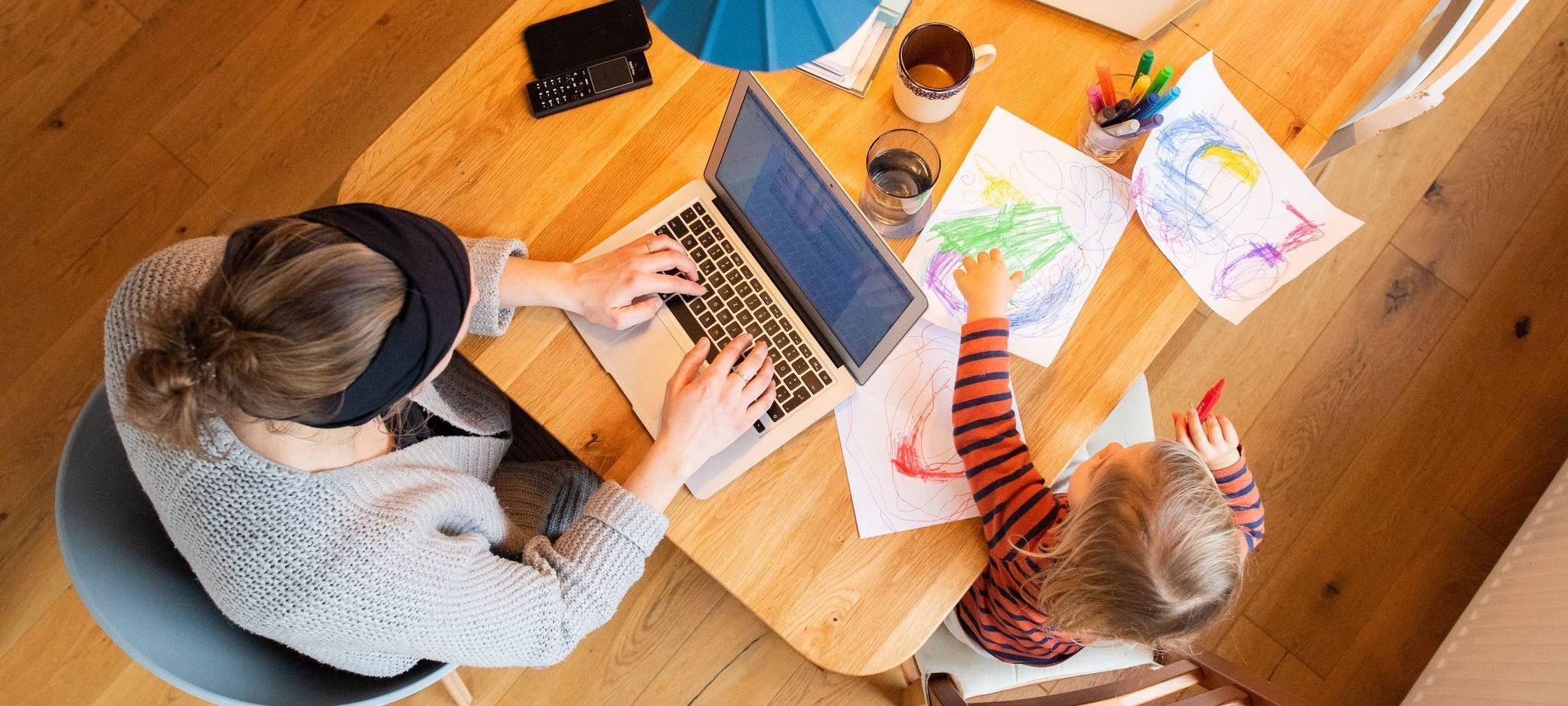 Eine Frau arbeitetneben ihrem Kind am Laptop